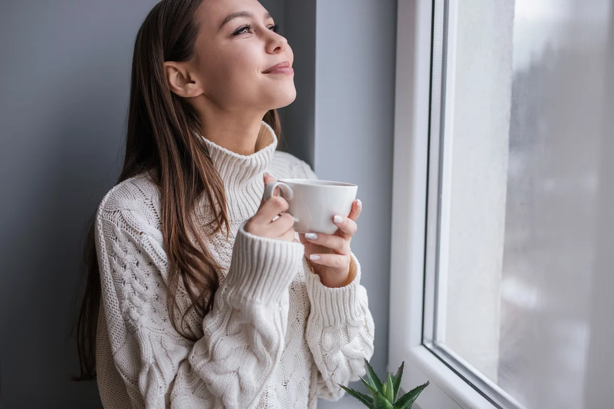 Une femme à sa fenêtre, une tasse entre les mains
